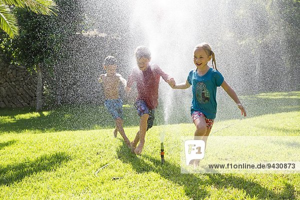Three children in garden running through water sprinkler