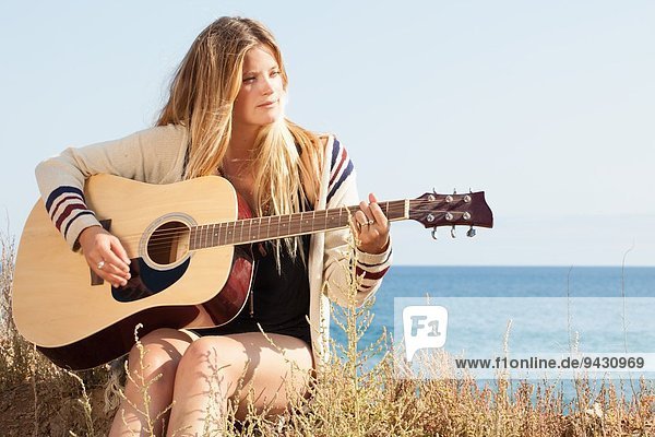 Young woman playing acoustic guitar at coast  Malibu  California  USA