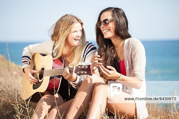 Zwei junge Frauen mit Akustikgitarre an der Küste  Malibu  Kalifornien  USA