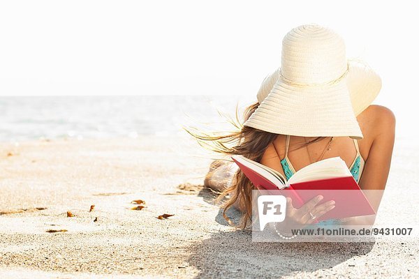 Young woman sunbathing and reading book on beach  Malibu  California  USA