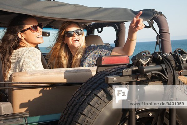 Two young women looking up from jeep at coast  Malibu  California  USA