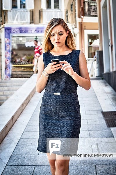 Ungeduldige junge Frau beim SMSen auf dem Smartphone in der Stadt.