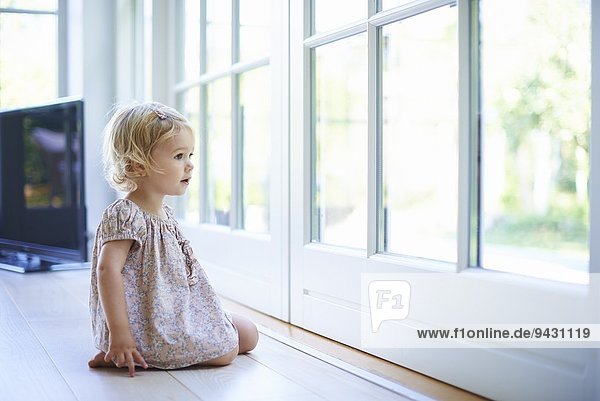 Portrait weibliches Kleinkind auf dem Boden sitzend mit Blick aus den Terrassentüren