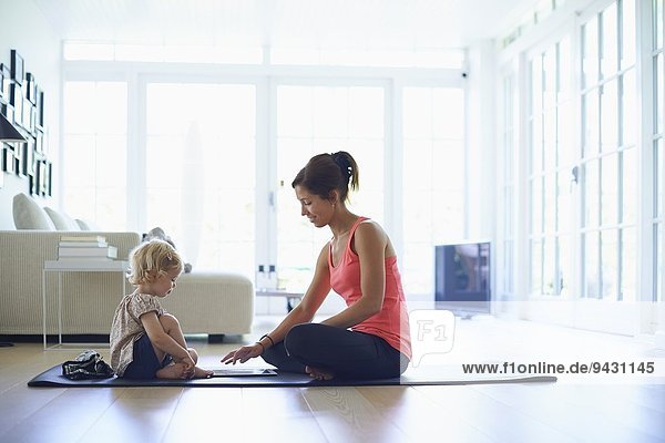 Mid adult mother and toddler daughter practicing yoga in living room