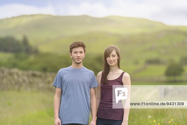 Junges Paar steht zusammen auf der Wiese und schaut weg über die ländliche Landschaft.