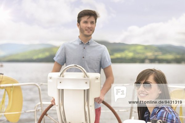 Junger Mann am Ruder der Yacht mit Freundin in Sonnenbrille