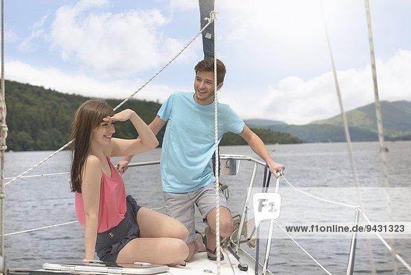 Young couple on bow of yacht sailing on lake under bright sunlight