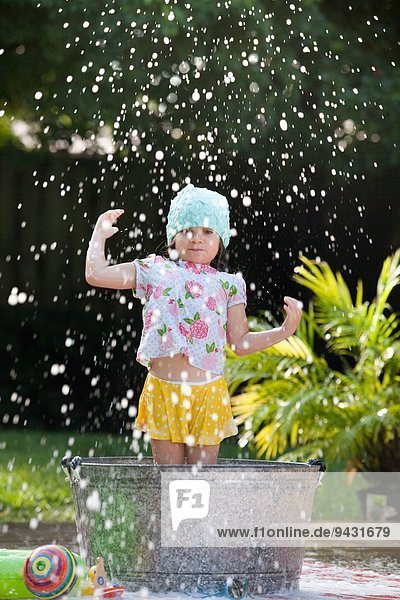 Mädchen steht im Schaumbad im Garten und spritzt Seifenblasen