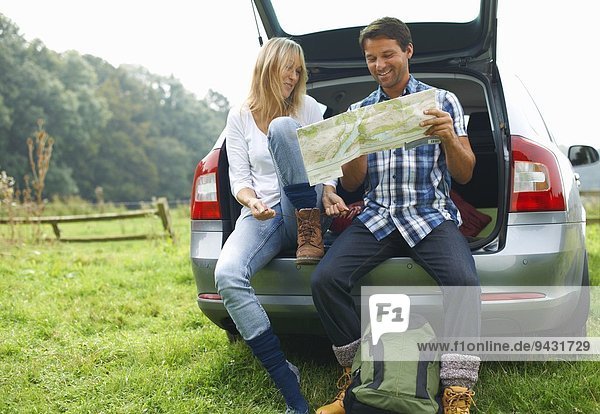 Couple at rear of car map reading preparing for walk