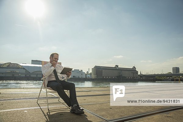 Geschäftsmann auf Stuhl auf Straßenbahnschienen sitzend mit Tablett