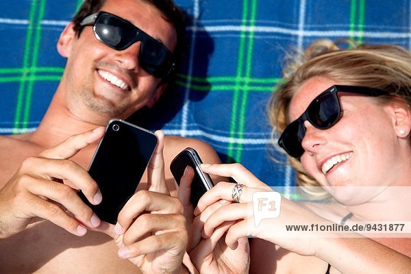 Junges Paar  das mit Smartphones auf dem Strandtuch liegt