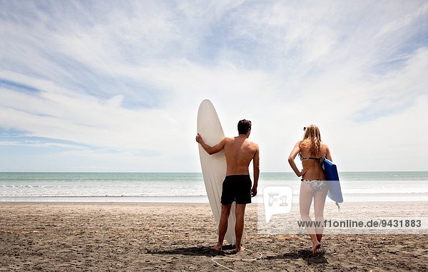 Young couple standing on beach holding surfboard and boogie board