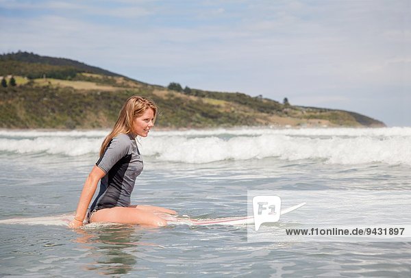 Portrait einer jungen Frau  die auf dem Surfbrett im Meer sitzt
