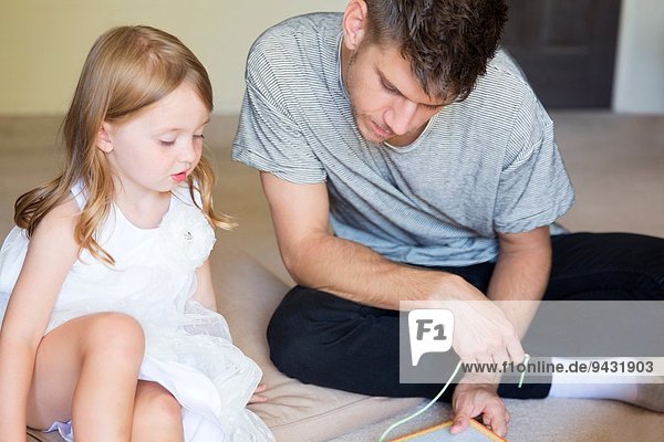 Junger Mann und Tochter beim Einfädeln des Bilderbuchs im Wohnzimmer