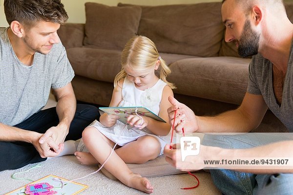 Male couple and daughter threading picture books on sitting room floor
