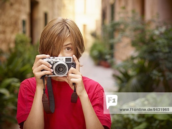 Porträt eines Jungen  der die Dorfstraße mit einer Spiegelreflexkamera fotografiert  Mallorca  Spanien