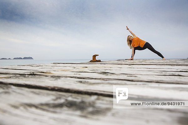 Mittlere erwachsene Frau praktiziert Yogastellung auf hölzernem Pier