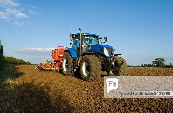 Farmer driving tractor and drilling seed corn in ploughed field