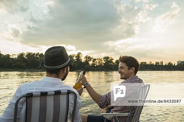 Young men toasting with beer bottles by lake