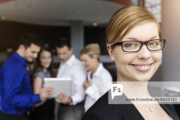 Lächelnde Geschäftsfrau  Kollegen im Hintergrund mit digitalem Tablett