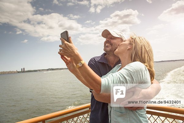 Mature couple photographing themselves on passenger ferry deck