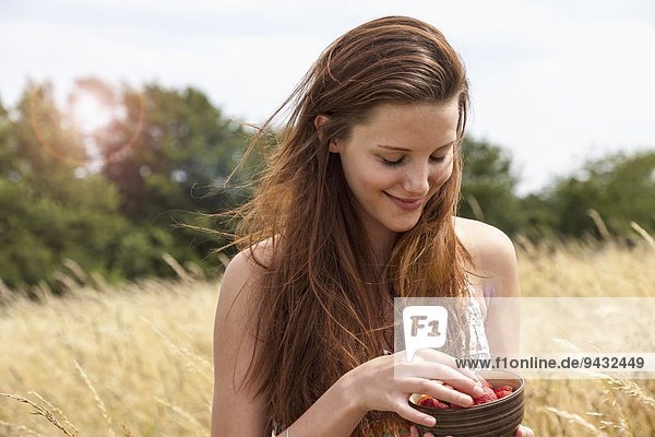 Junge Frau hält Schale mit frischem Obst im Feld