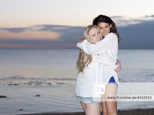 Portrait of two young women friends hugging on beach at dusk  Williamstown  Melbourne  Australia