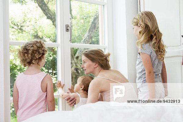 Mutter und drei Töchter schauen aus dem Fenster.