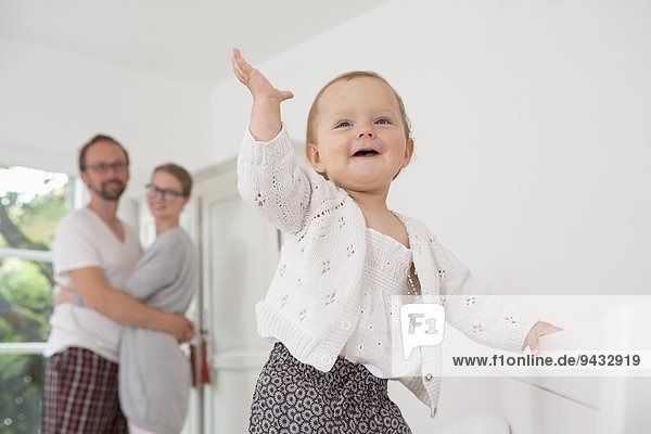 Baby mit erhobener Hand  Eltern im Hintergrund