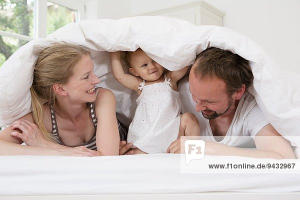 Eltern spielen mit der kleinen Tochter unter der Bettdecke