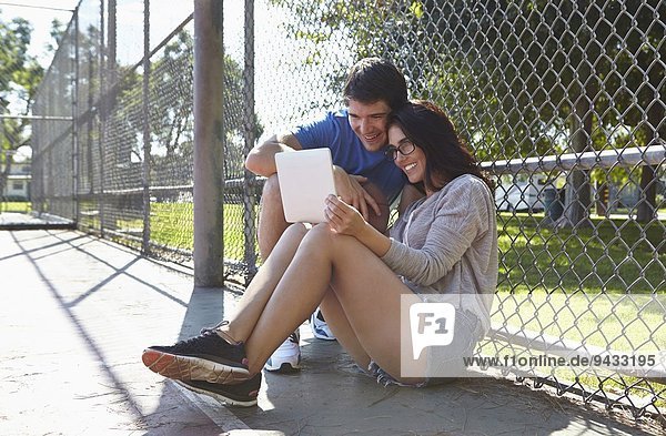 Junges Paar mit digitalem Tablett am Drahtzaun