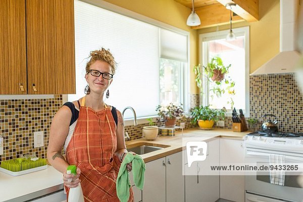 Junge Frau reinigt Küche mit grünen Reinigungsmitteln