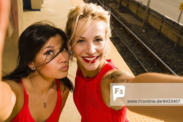 Zwei junge Frauen nehmen Selfie auf dem Bahnsteig.