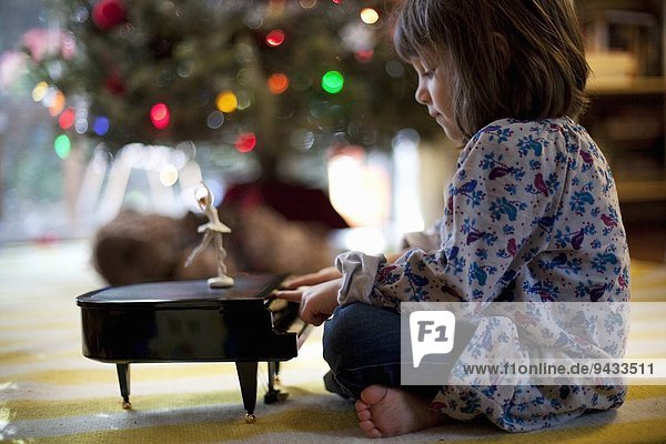 Mädchen sitzt auf dem Wohnzimmerboden und spielt Spielzeug Klavierspieluhr zu Weihnachten.