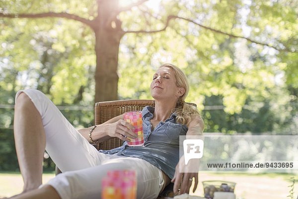 Reife Frau entspannt im Garten mit Getränk