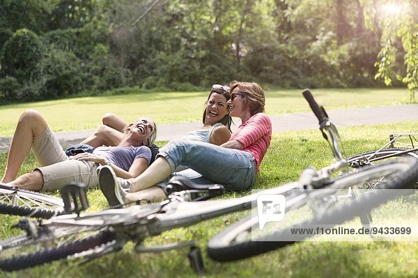 Three mature woman relaxing on grass after bicycle ride