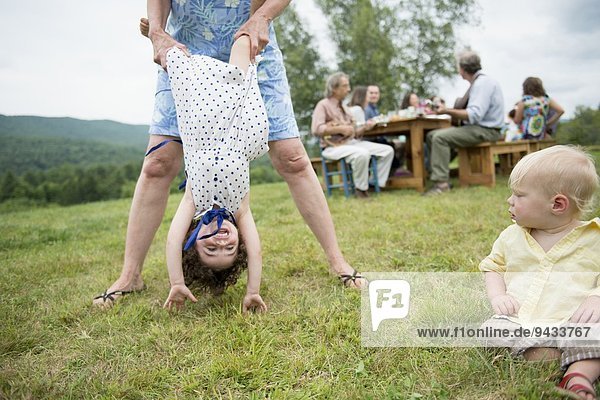 Weibliches Familienmitglied hält spielerisch Kleinkind an den Beinen beim Familientreffen im Freien.
