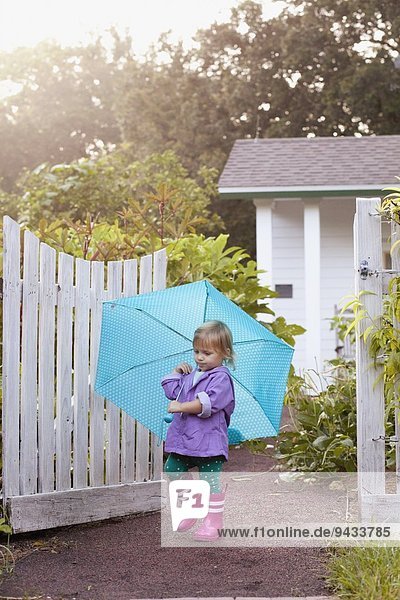 Weibliches Kleinkind beim Spaziergang im Garten mit Regenschirm