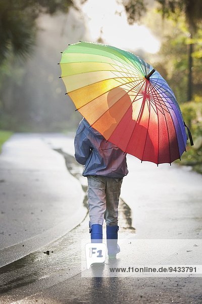 Rückansicht des Jungen mit Regenschirm auf der Straße