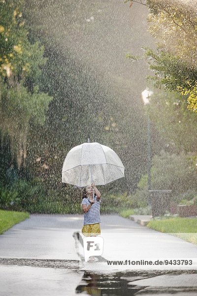 Barfuss-Mädchen hält Regenschirm hoch und läuft durch Pfützen auf der Straße.