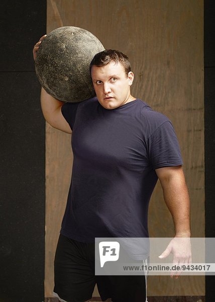 Portrait eines jungen Gewichthebers mit Atlasball auf der Schulter in der Turnhalle
