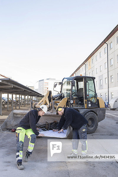 Arbeiter analysieren Bauplan vor dem Bagger auf der Baustelle