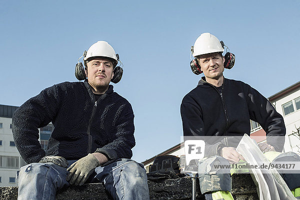 Porträt der selbstbewussten Arbeiter auf der Baustelle gegen den klaren blauen Himmel