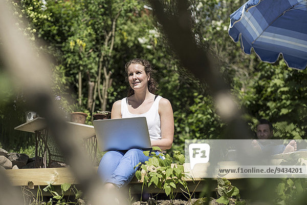 Lächelnde mittlere erwachsene Frau mit Laptop auf der Terrasse sitzend