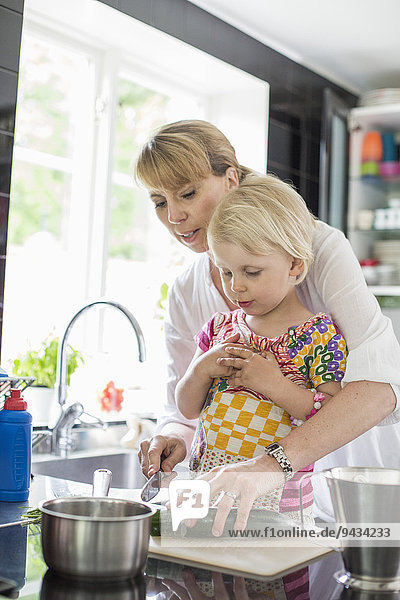 Mother teaching daughter to cut vegetables in kitchen