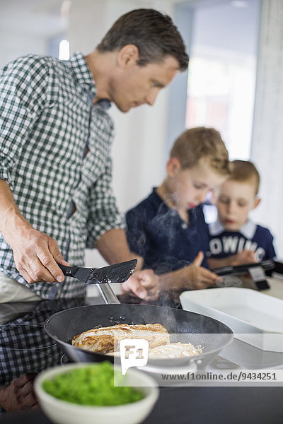Father looking at sons using digital tablet while preparing food in kitchen