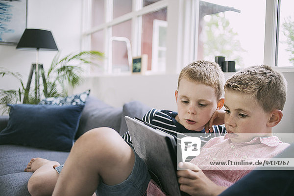 Brüder  die zu Hause ein digitales Tablett auf dem Sofa benutzen