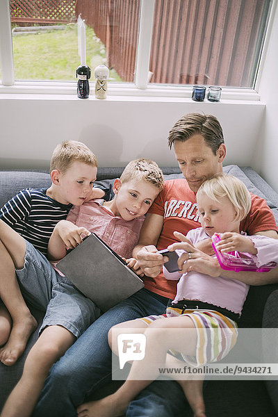 Father and children using technologies on sofa at home