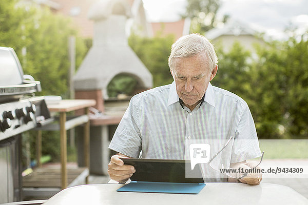 Senior Mann mit digitalem Tablett am Tisch im Hof