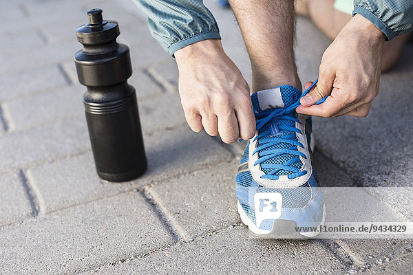 Niedriger Abschnitt des Mannes,  der Sport-Schnürsenkel durch eine Wasserflasche auf der Straße bindet.